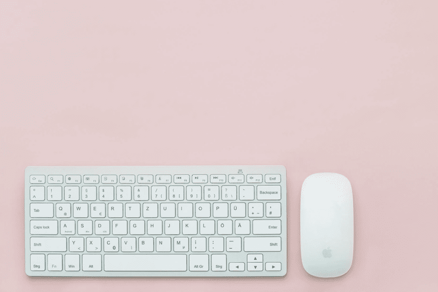 white keyboard and white computer mouse on pink desktop with no clutter